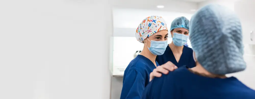 Three healthcare professionals in surgical caps and masks in a clinical setting